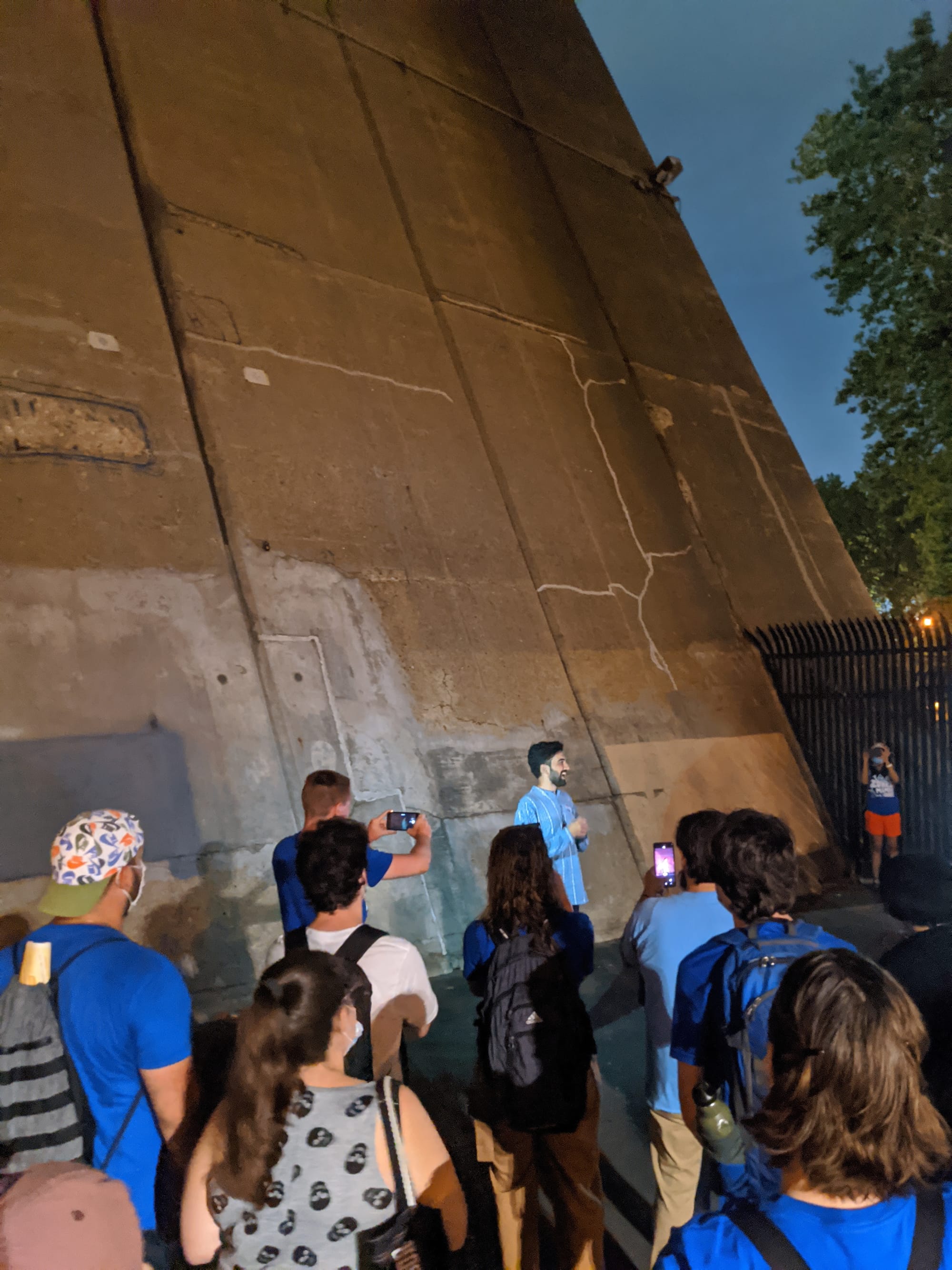 a small crowd facing Zohran Mamdami who has a blue top and is speaking.